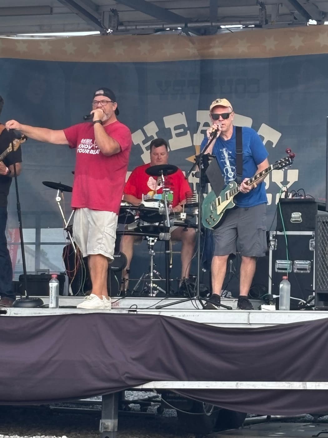 Singer, drummer, and guitarist mid-set on the outdoor stage